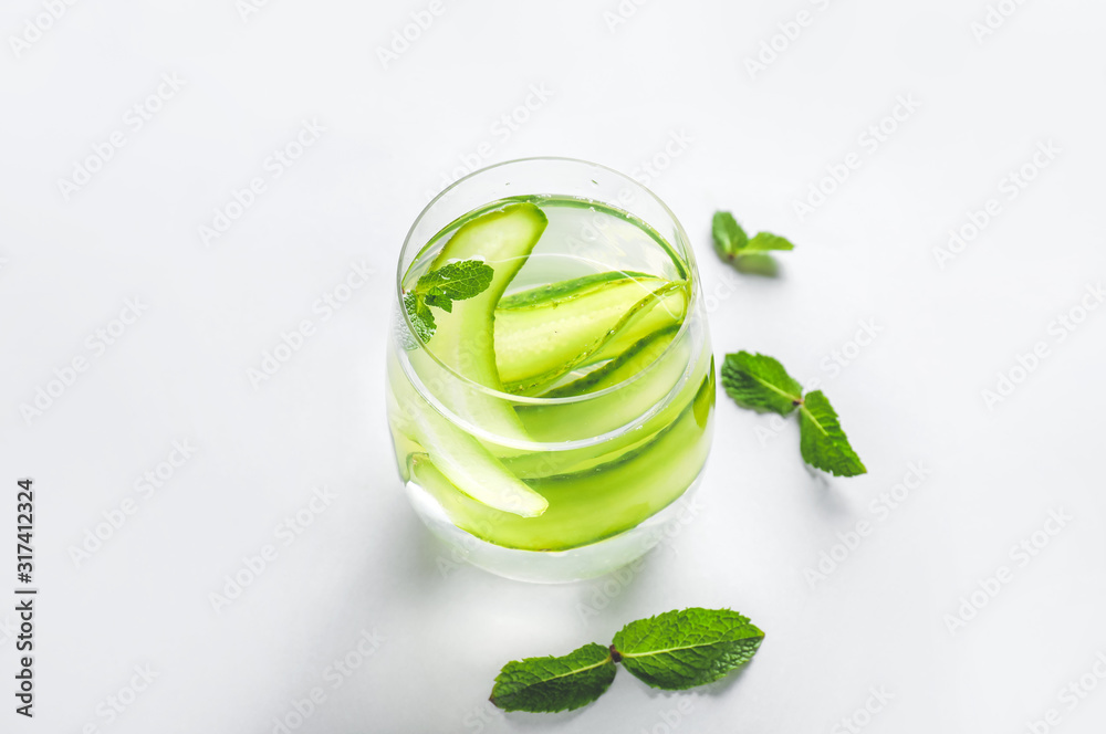 Glass of cold cucumber water on light background