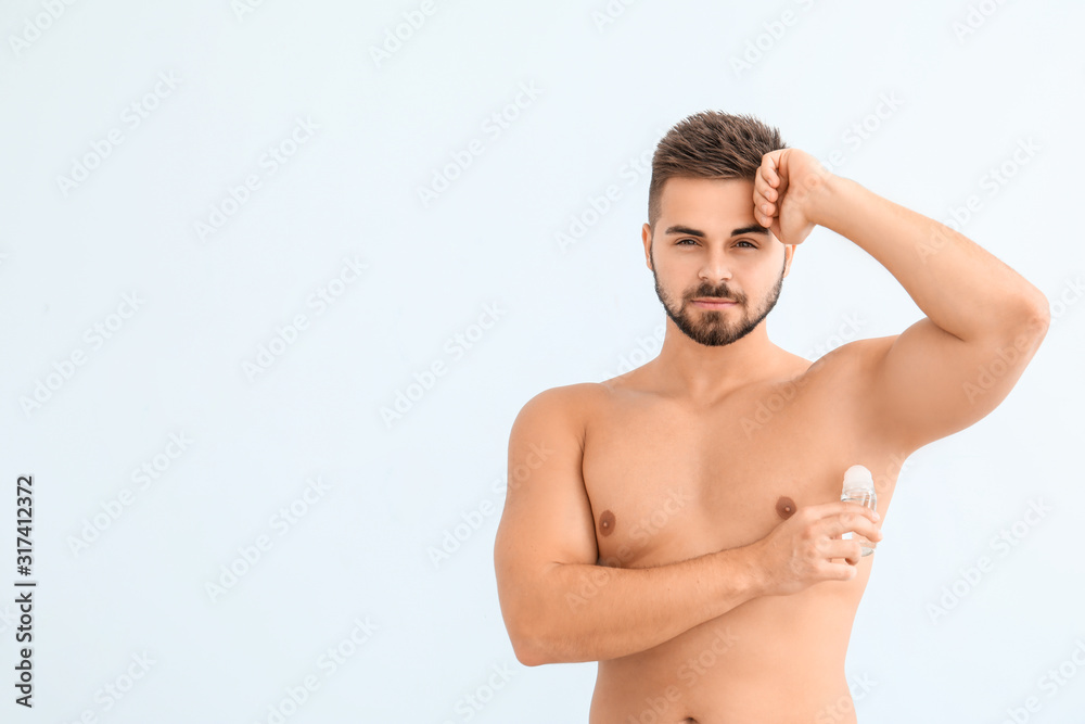 Handsome young man using deodorant on color background