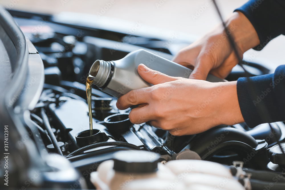 Male mechanic refilling car oil in service center