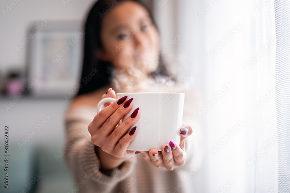 家里的亚洲女人手里拿着一杯茶或咖啡