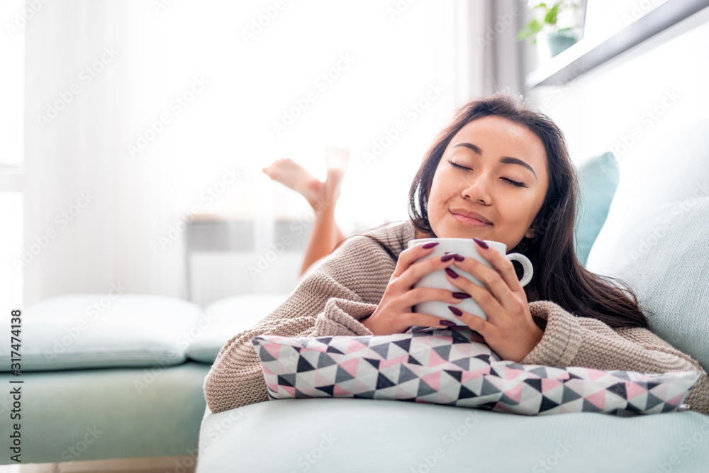 Happy asian girl lying on sofa with cup of coffee at home