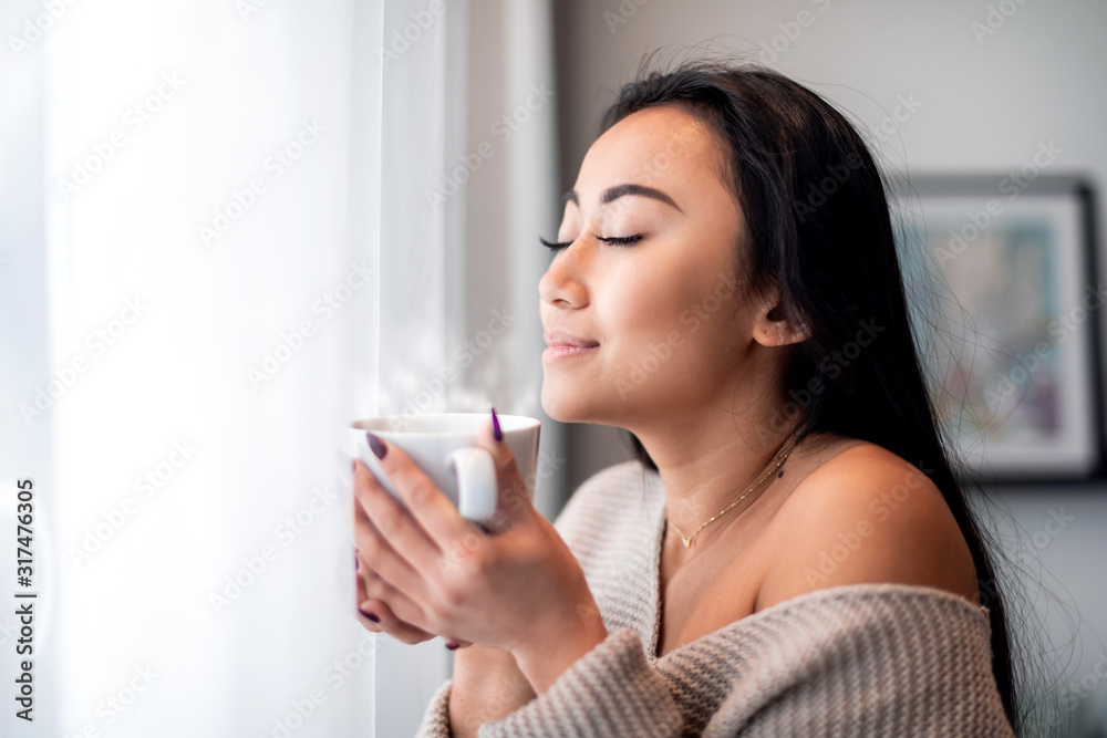 悠闲的亚洲女人在家里喝杯茶或咖啡度过休闲时光