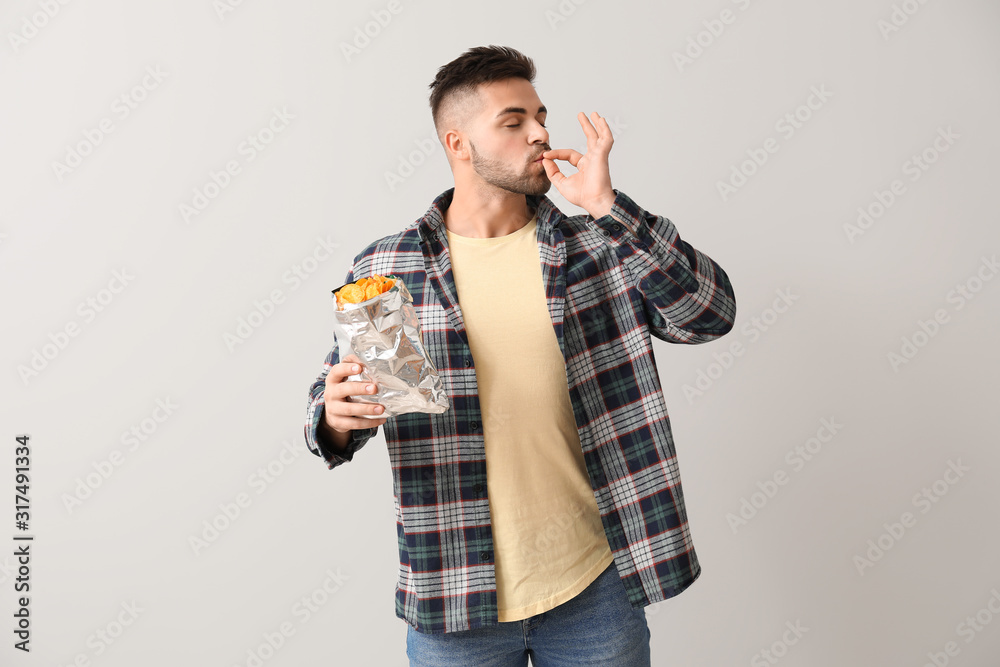 Handsome young man with tasty potato chips on light background