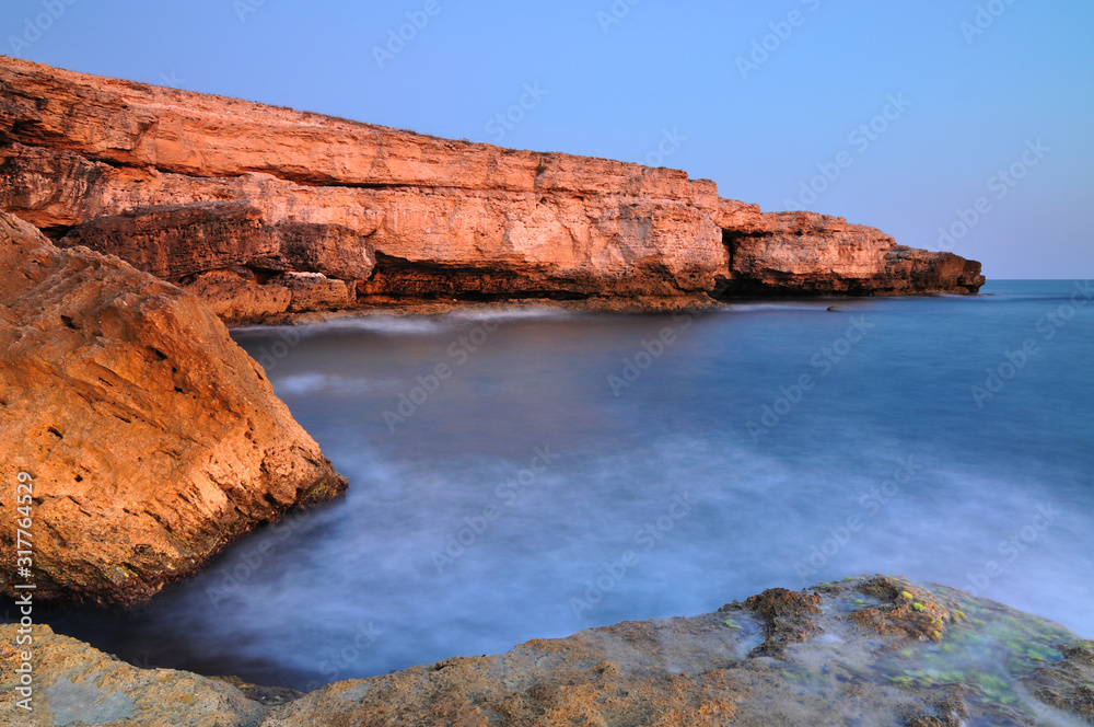 一名男子站在黑海海岸线上的岩石上，海水清澈，天空湛蓝