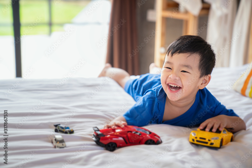 Asian boy fun and play a car toy on the bed