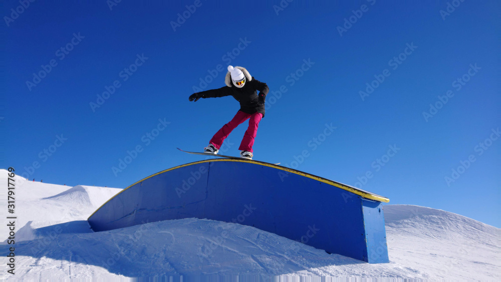 酷酷的女单板滑雪运动员在一个大型雪上公园里沿着栏杆做吊臂动作。