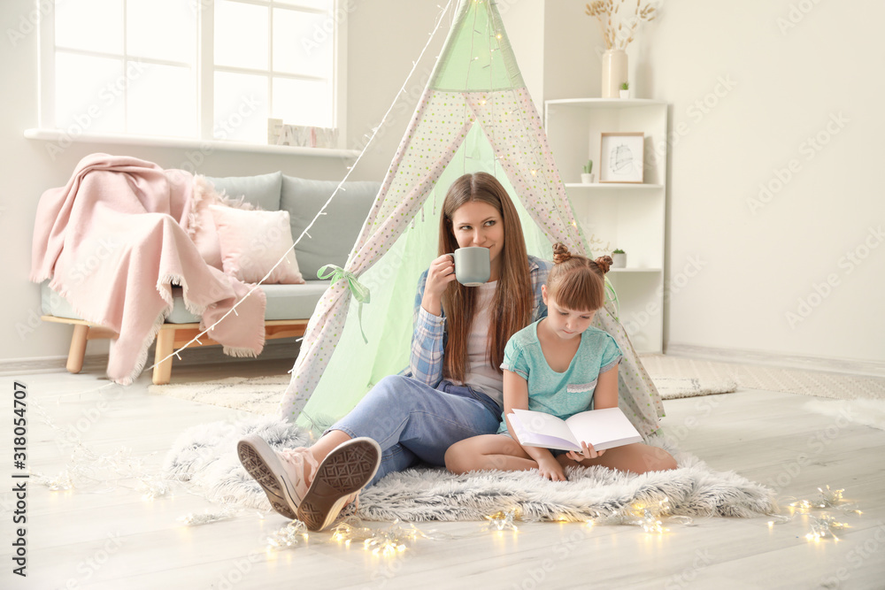 Beautiful young woman and her little daughter reading book at home