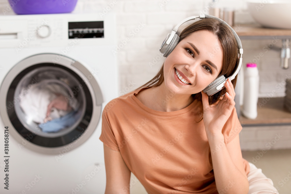 Young housewife listening to music while washing laundry at home