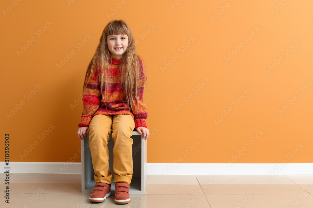 Cute little girl in autumn clothes sitting near color wall