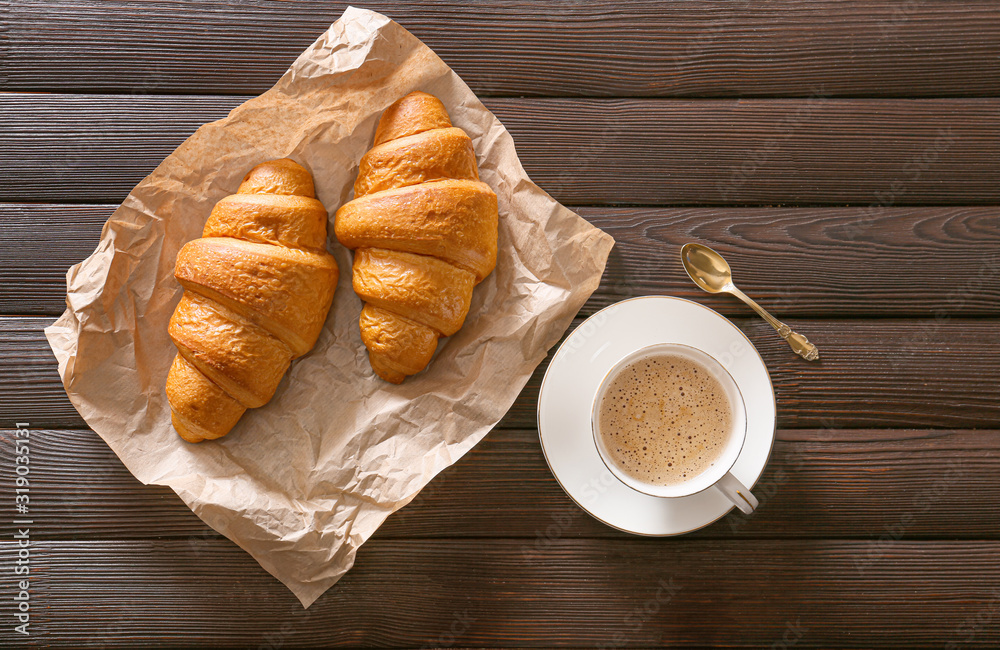 Parchment with tasty croissants and cup of coffee on table