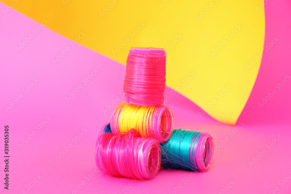 Hair curlers with colorful strands on bright background