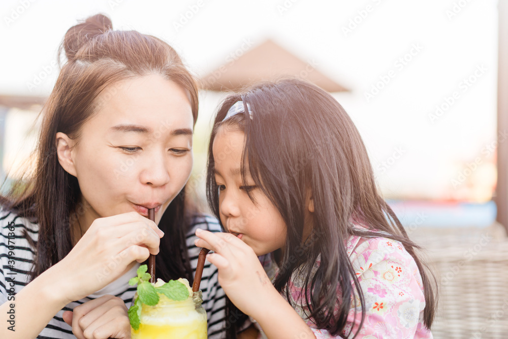 快乐大笑的小女孩和她年轻漂亮的妈妈一起喝新鲜的菠萝奶昔