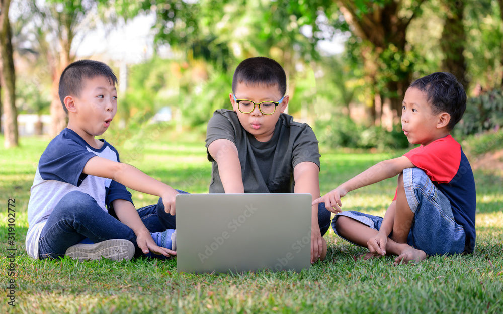 一群多民族小学生坐在操场草地上看着笔记本电脑