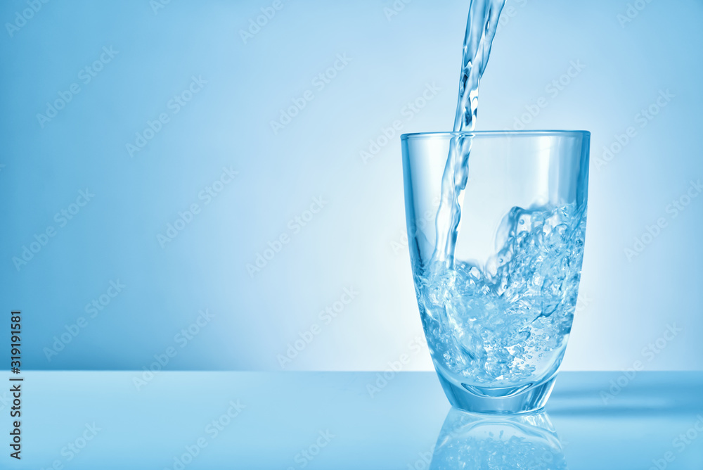 Pouring of fresh water into glass on color background