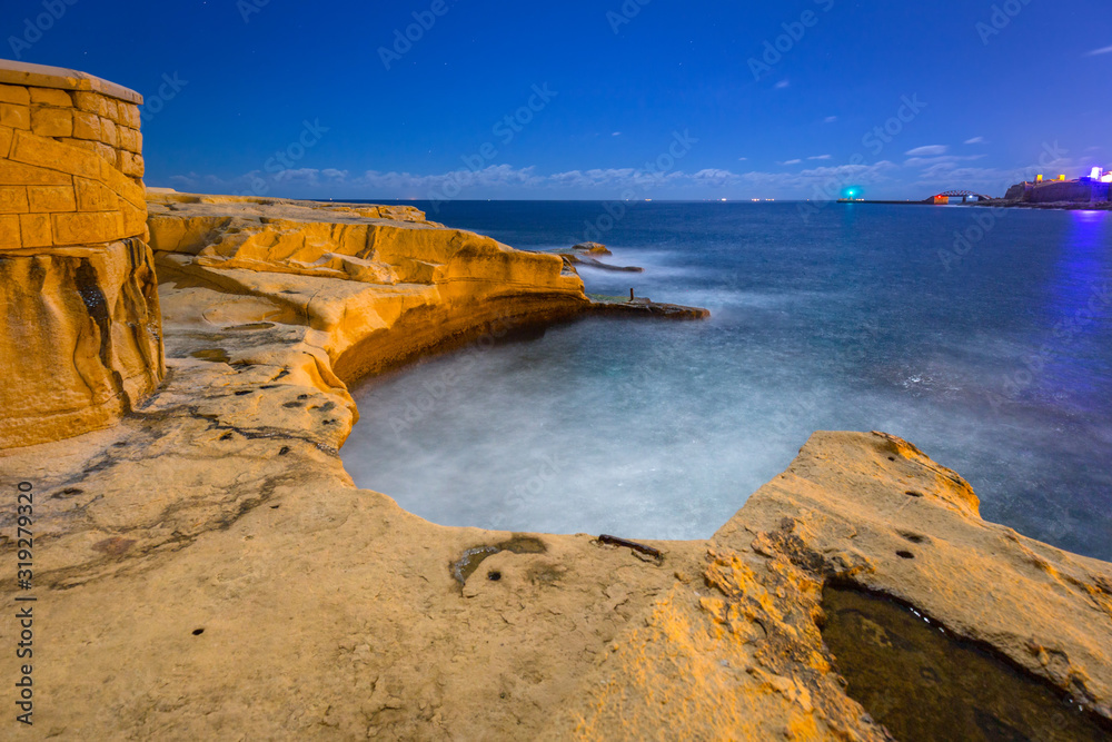 Rocky coastline of Malta at night illuminated by moonlight