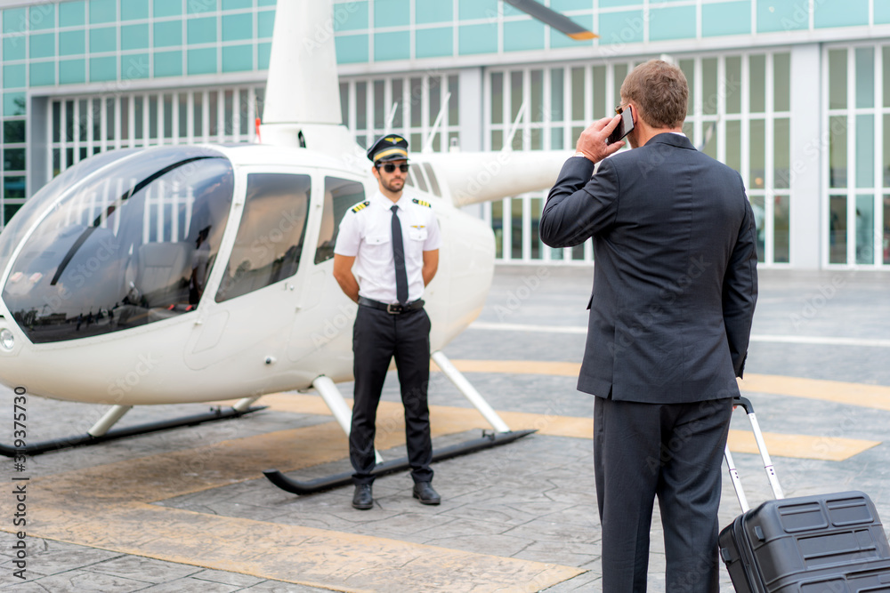 Elderly Businessman manager with Luggage talking mobile phone and walking to helicopter to departure