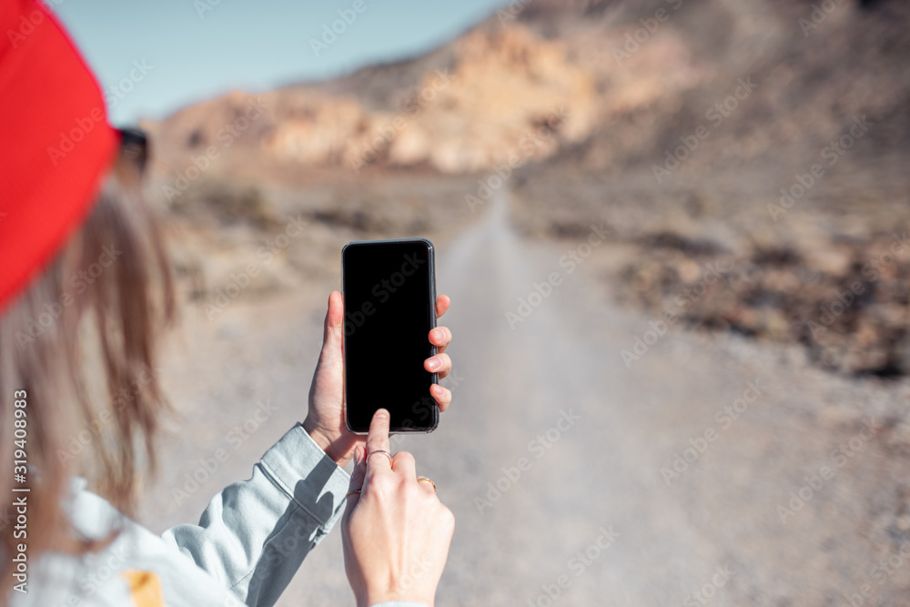 背景是沙漠公路的智能手机实物模型。女人带着手机旅行