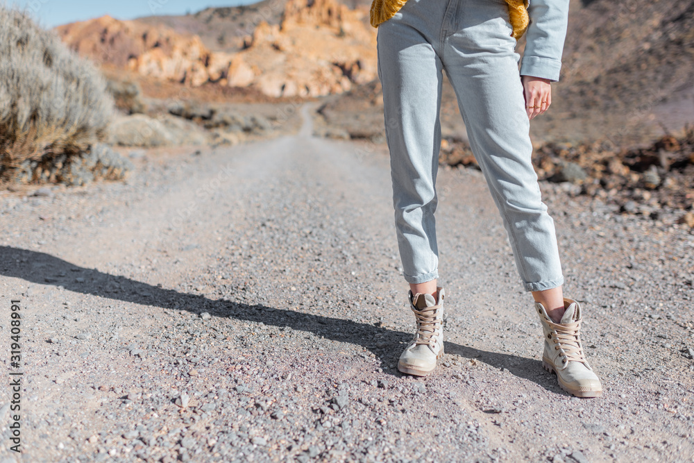 Woman in jeans and trekking shoes on the desert road, close-up view on the legs. Travel concept