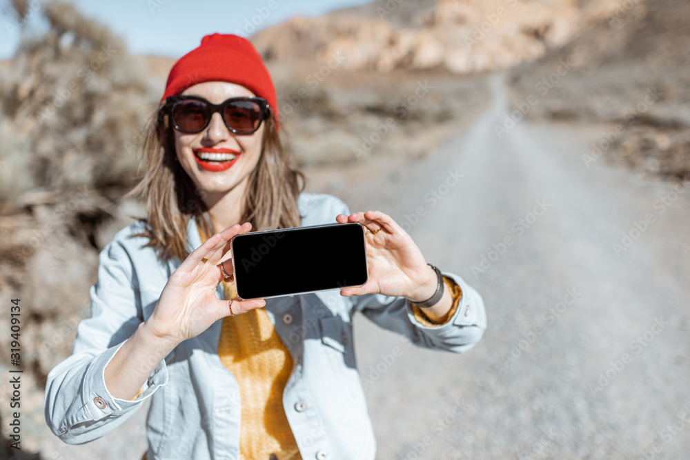 Young and happy woman showing smartphone with empty screen to copy paste while traveling on the dese