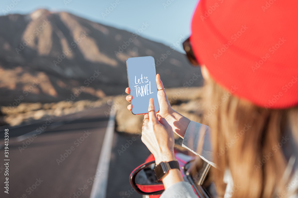 在火山谷上开车旅行的女人，从车窗探出头，手里拿着智能手机。