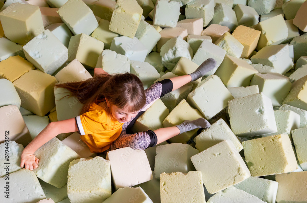 Child girl having fun while jumping to soft box pool in trampoline center