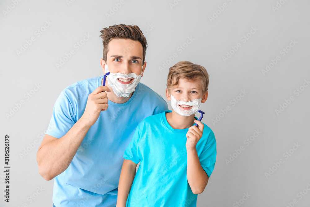 Father and his little son shaving against grey background