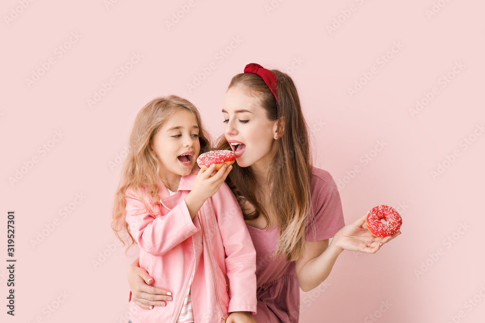 Cute mother and little daughter with tasty donuts on color background