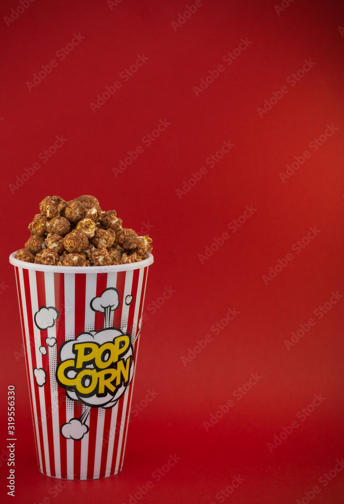 Butter popcorn in a red popcorn cup, snack in the house or cinema on a red background