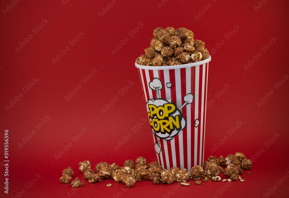 Butter popcorn in a red popcorn cup, snack in the house or cinema on a red background