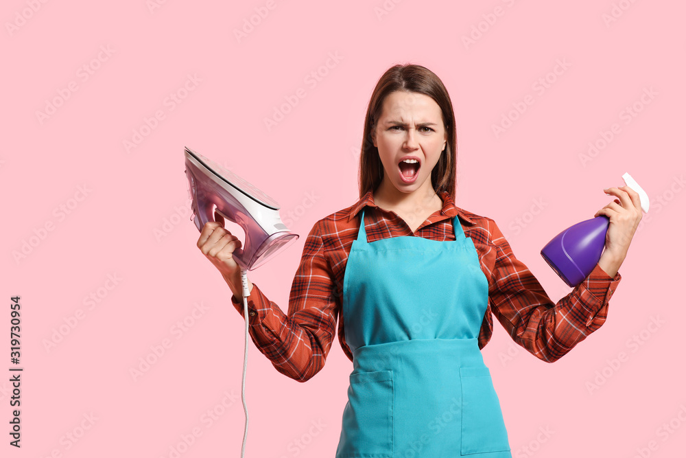 Aggressive young housewife with iron and detergent on color background