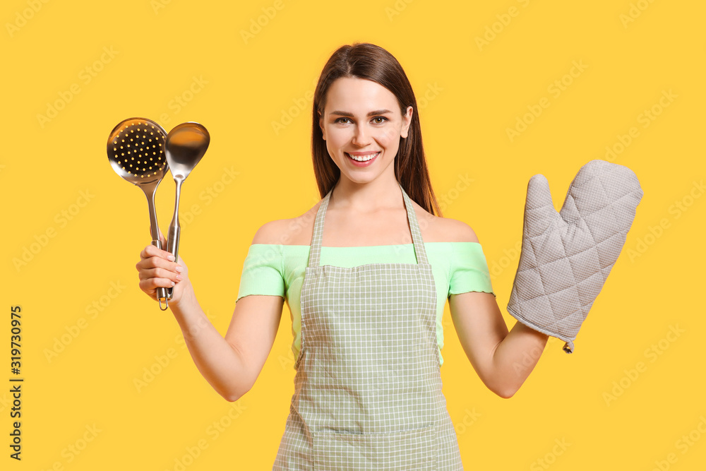 Young housewife with kitchenware on color background