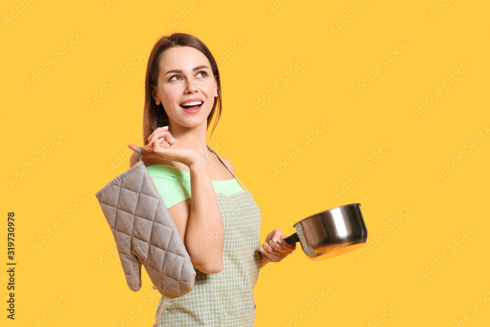 Young housewife with kitchenware on color background