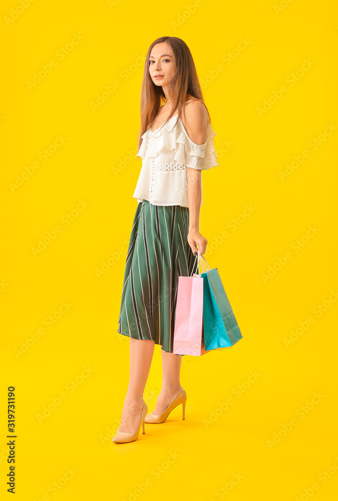 Beautiful young woman with shopping bags on color background