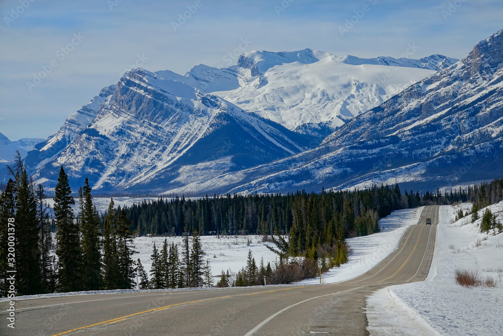 AERIAL: Scenic view of the snowy Rockies as car disappears in the distance.