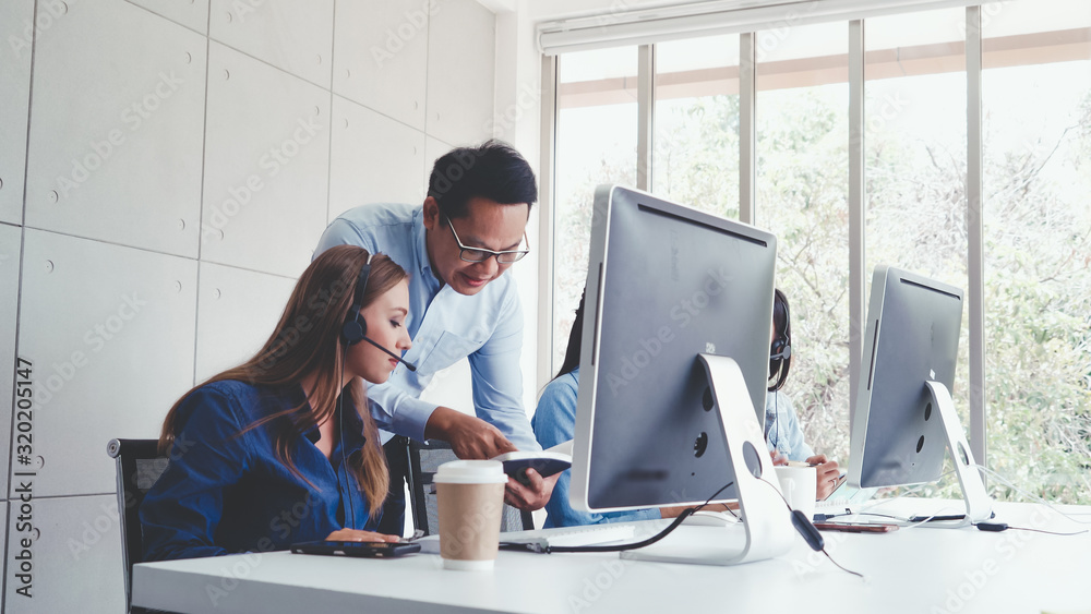 Customer support agent or call center with headset works on desktop computer while supporting the cu