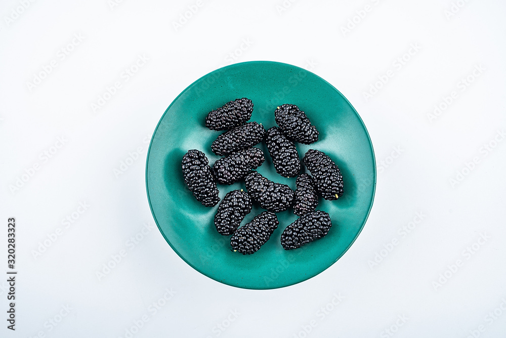 Dark green tall plate filled with fresh mulberries on white background