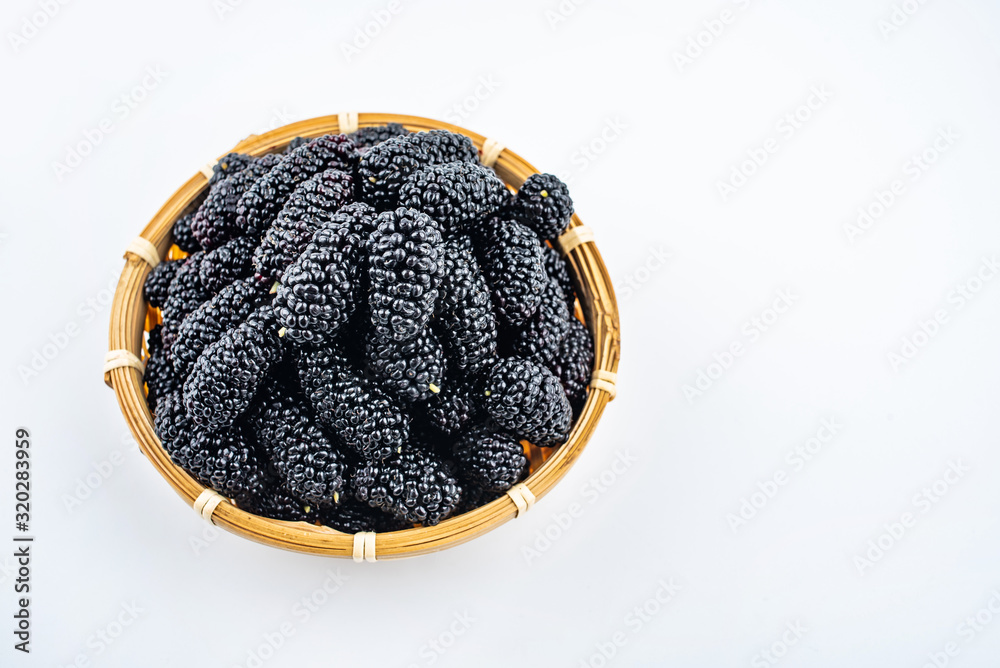 A bamboo dish filled with fresh black mulberries on a white background