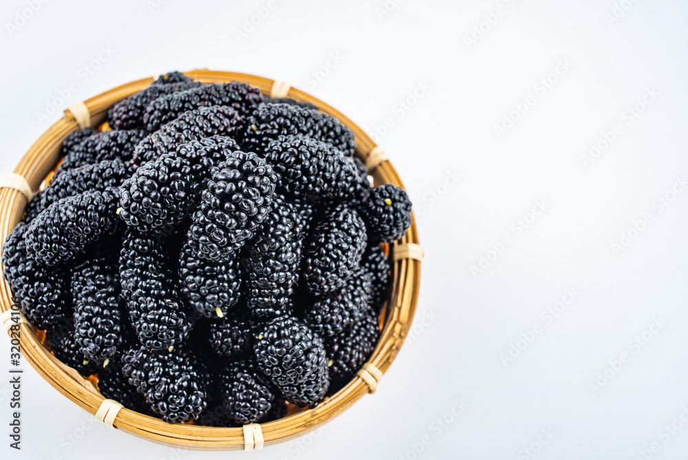 A bamboo dish filled with fresh black mulberries on a white background