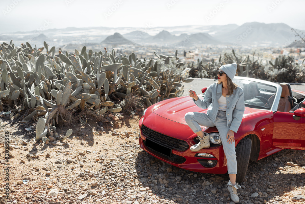 Young woman dressed casually with hat enjoying road trip on the island, standing with phone near the