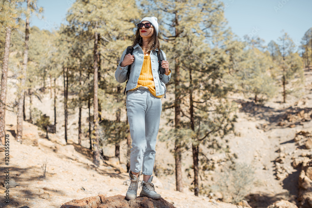 Portrait of a stylish woman enjoying beautiful landscapes on volcanic rocks in the pine woods, trave