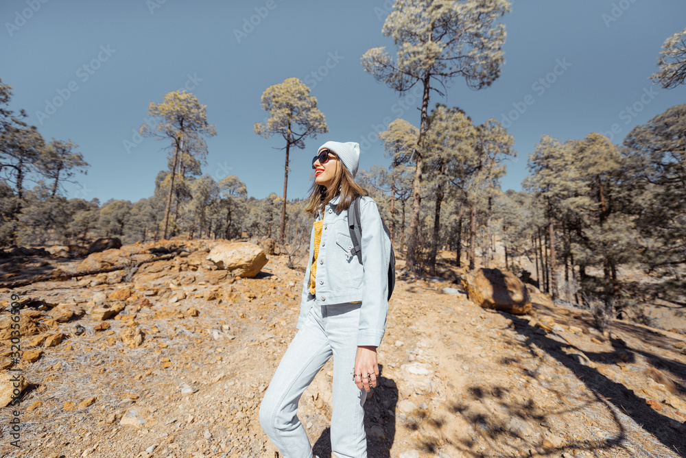 Young woman dressed casually walking with backpack in the forest highly in the mountains on the volc