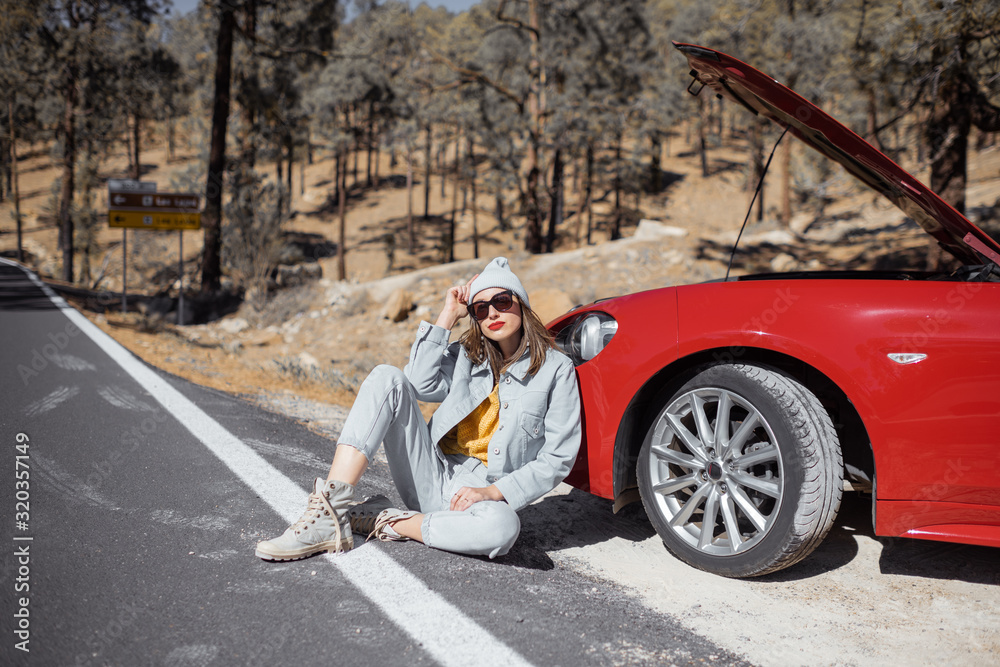 Frustrated woman sitting on the roadside, having some problems with a car while traveling alone at t