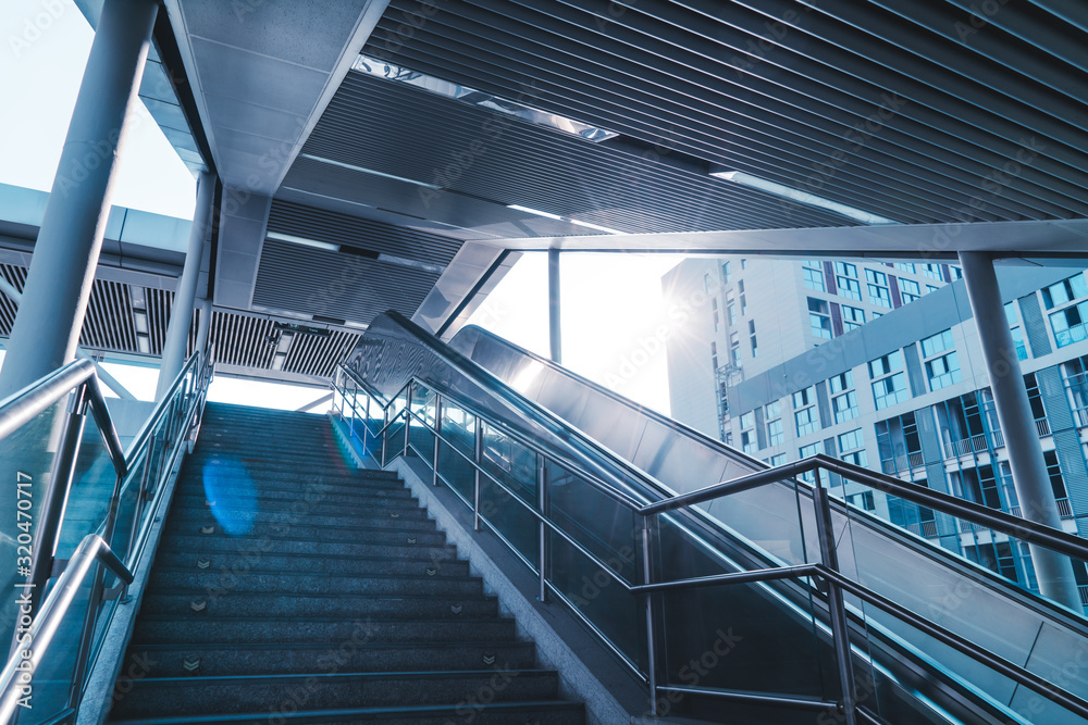 Outdoor elevators and city buildings, with sunlight in front.