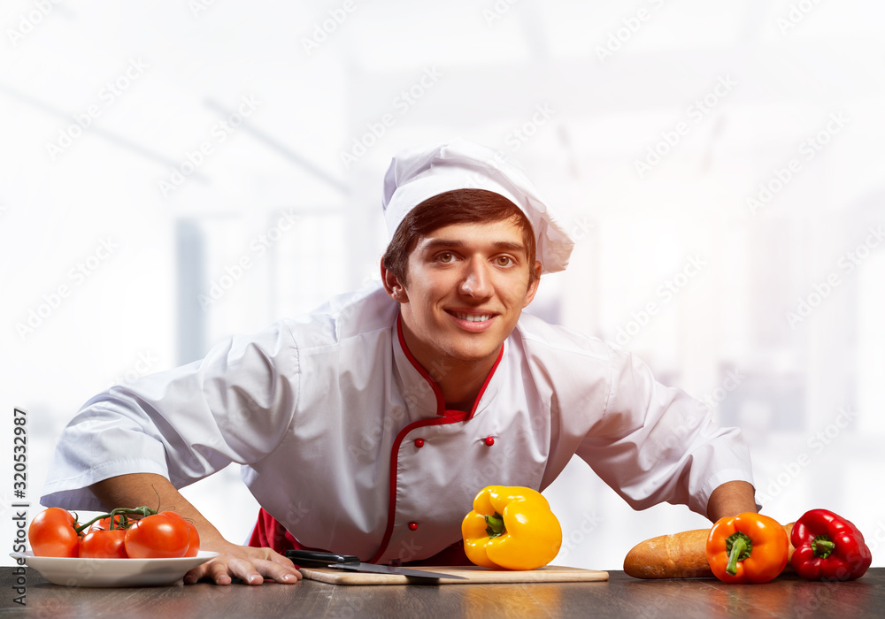 Young smiling chef standing near cooking table