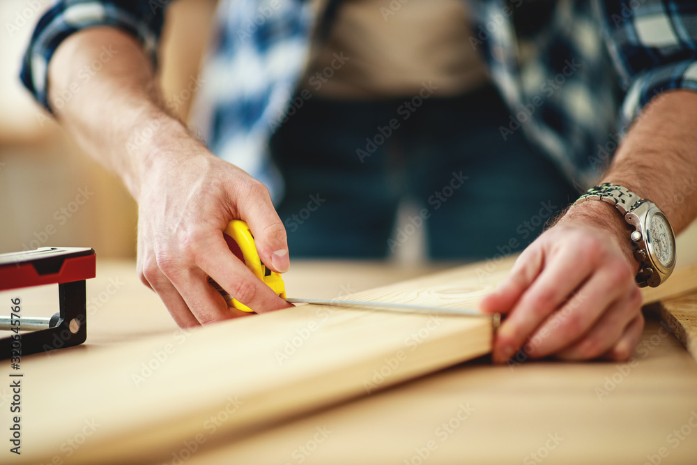 .    carpenters hands with tape measure and pencil measure wooden Board