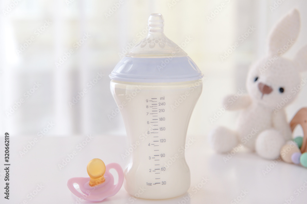 Bottle of milk for baby with pacifier on table indoors