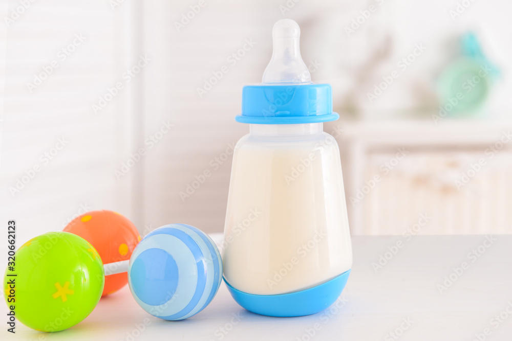 Bottle of milk for baby with toy on table indoors