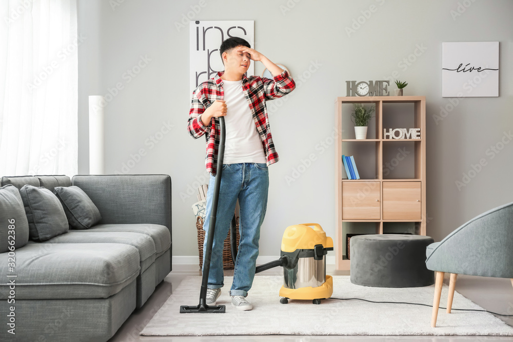 Tired Asian man with vacuum cleaner at home