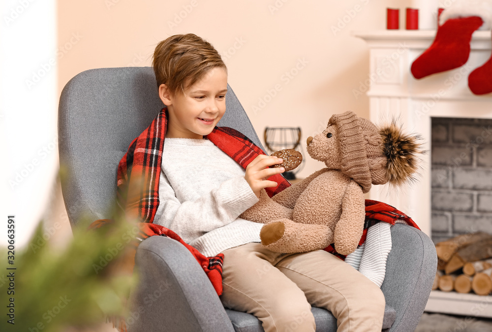 Cute little boy with teddy bear and cookie on Christmas eve at home