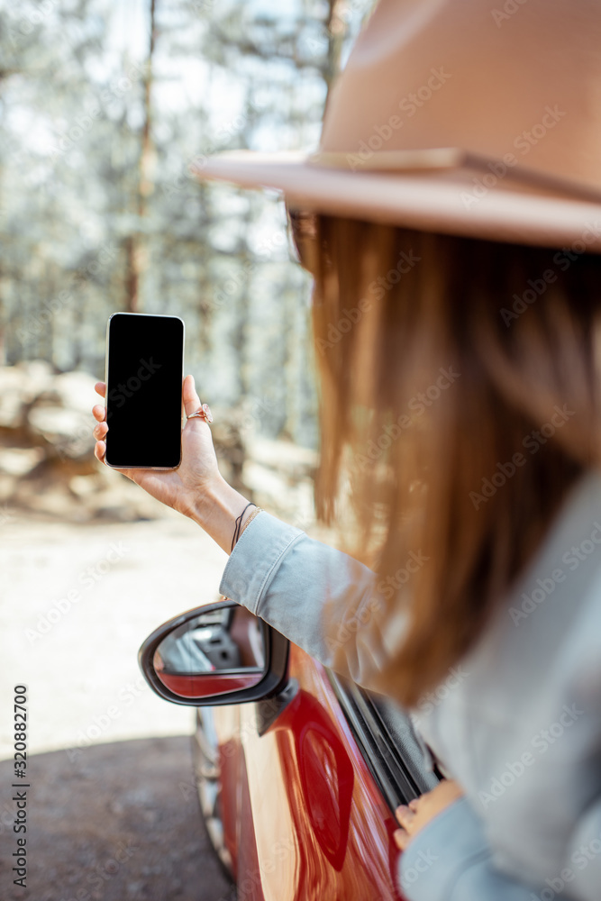 Woman traveling by car in the forest, leaning out of the car window and photographing with a smart p